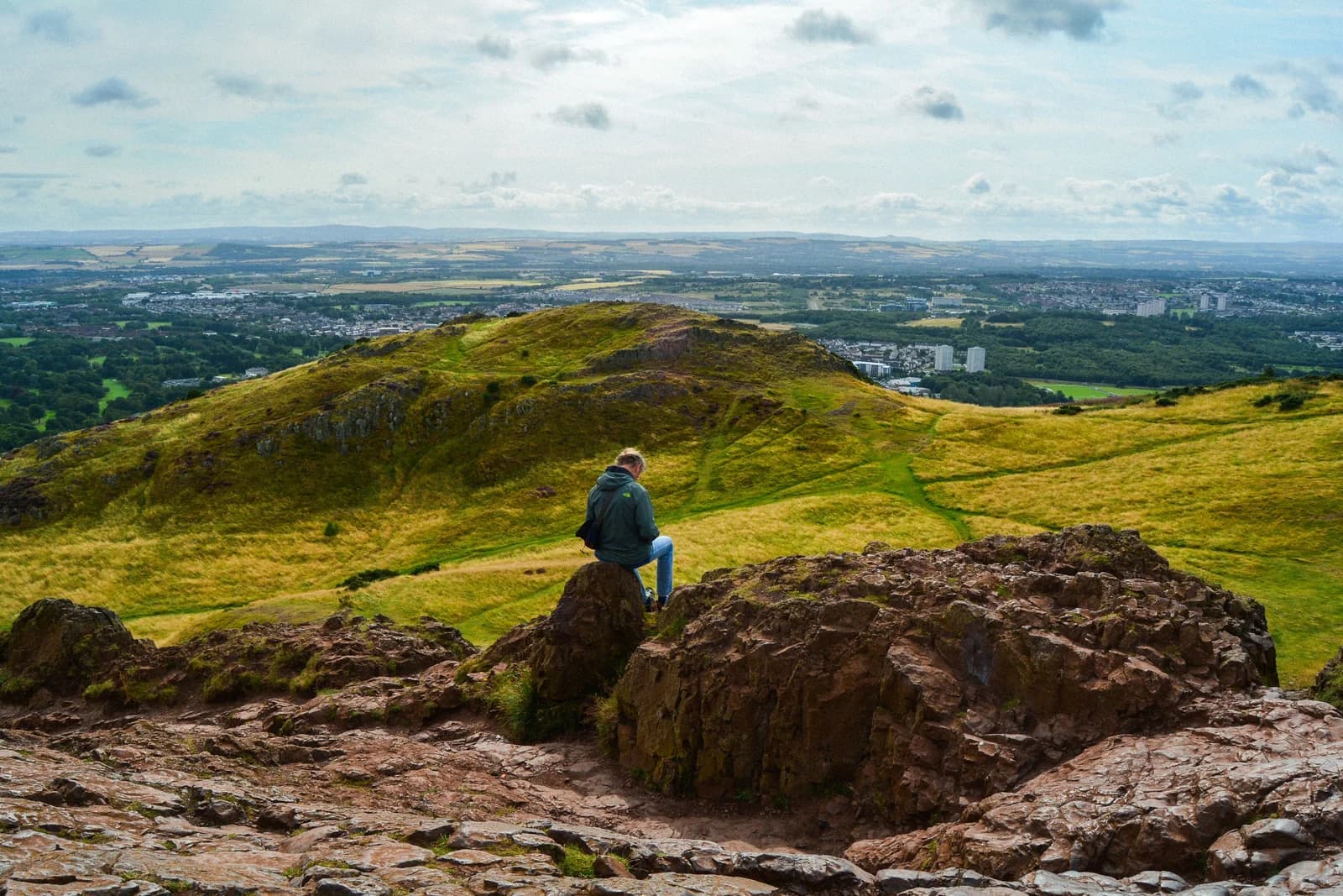 A hiker on Arthur's Seat looking over Edinburgh's historic center and rooftops